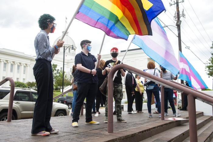 demonstrators in support of transgender rights hold flags during a rally outside the Alabama State House in Montgomery, Ala.