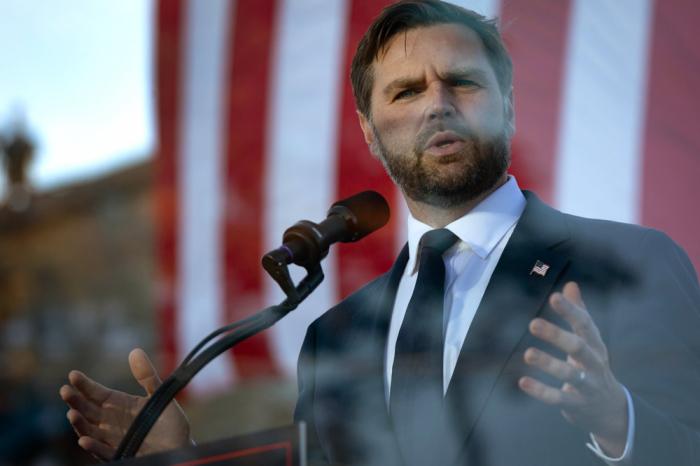 Behind a bullet-proof barrier, Republican vice presidential nominee, U.S. Sen. J.D. Vance (R-OH) speaks at a rally on the grounds of the Berlin Raceway on October 02, 2024 in Marne, Michigan. Republican presidential nominee former President Donald Trump i