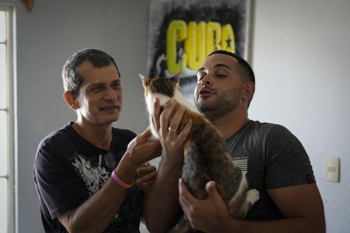 Partners Lázaro "Lachi" González, left, and Adiel González play with their cat Zaida, on the sidelines of an interview at their home in Matanzas, Cuba.