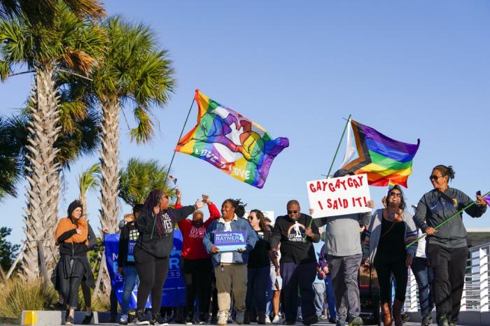 Marchers wave flags as they walk at the St. Pete Pier during a rally and march to protest against a bill dubbed by opponents as the "Don't Say Gay" bill Saturday, March 12, 2022, in St. Petersburg, Fla.