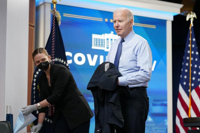 President Joe Biden removes his jacket before receiving his second COVID-19 booster shot in the South Court Auditorium on the White House campus.