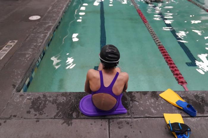 A 12 year old transgender swimmer is seen waiting by a pool.