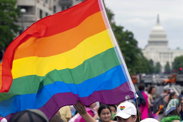 With the U.S. Capitol in the background, a person waves a rainbow flag as they participant in a rally in support of the LGBTQIA+ community at Freedom Plaza, in Washington. 