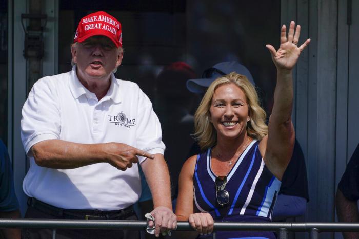 Rep. Marjorie Taylor Greene, R-Ga., waves while former President Donald Trump points to her while they look over the 16th tee during the second round of the Bedminster Invitational LIV Golf tournament in Bedminster, N.J.