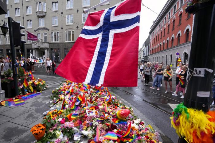 A Norwegian national flag flutters over flowers and rainbow flags that are placed at the scene of a shooting in central of Oslo, Norway,