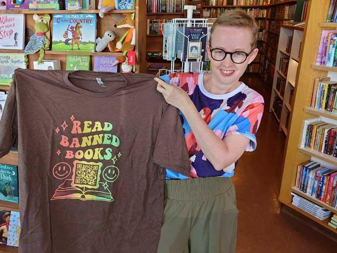 Former Norman High School English teacher Summer Boismier holds up a T-shirt with a QR code link to the Brooklyn Public Library at the Green Feather Book Company in Norman, Okla., on Oct. 6, 2022