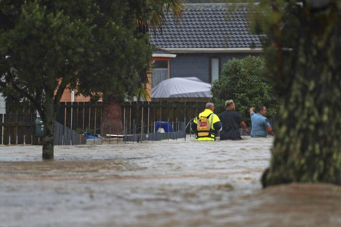 Emergency workers and a man wade through flood waters in Auckland, New Zealand, Friday, Jan. 27, 2023.