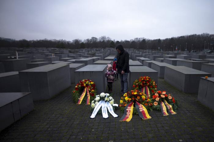 A father with his two kids stay behine wreaths, placed at the Memorial to the Murdered Jews of Europe on the International Holocaust Remembrance Day in Berlin, Germany, Friday, Jan. 27, 2023.