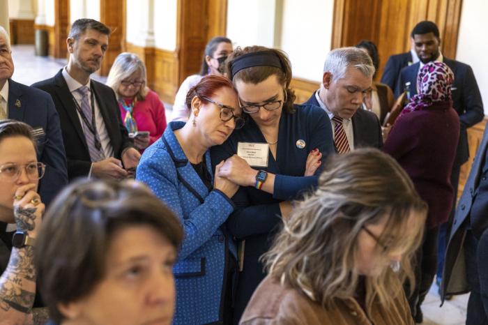 Jennifer Bowie, center left, and Aaron Baker, center right, become emotional while watching discussion of SB 140 on a video monitor in the Capitol before it gets final approval at the state Senate in Atlanta, Tuesday, March 21, 2023.