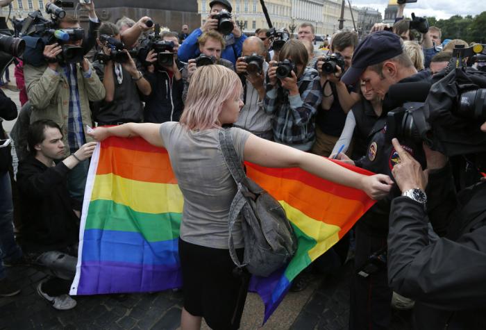 A gay rights activist stands with a rainbow flag, in front of journalists, during a protesting picket at Dvortsovaya (Palace) Square in St. Petersburg, Russia, on Aug. 2, 2015. 