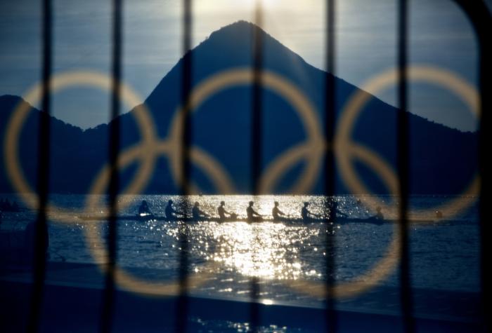 Rowers are seen through a screen decorated with the Olympic rings as they practice at the rowing venue in Lagoa at the 2016 Summer Olympics in Rio de Janeiro, Brazil, on Aug. 7, 2016.