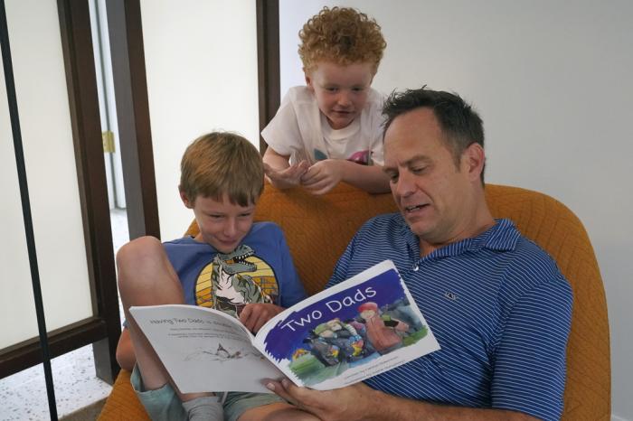 Wes Brown, right, reads to children Shawn Larimer-Brown, 7, left, and Charlie Larimer-Brown, 5, center, at their home Friday, Aug. 18, 2023, in Winter Park, Fla.