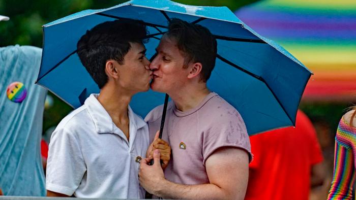 Jon Batayola, left, and Daniel Biginton embrace under an umbrella as they await the beginning of Chicago's annual Pride Parade, June 25, 2023, in Chicago