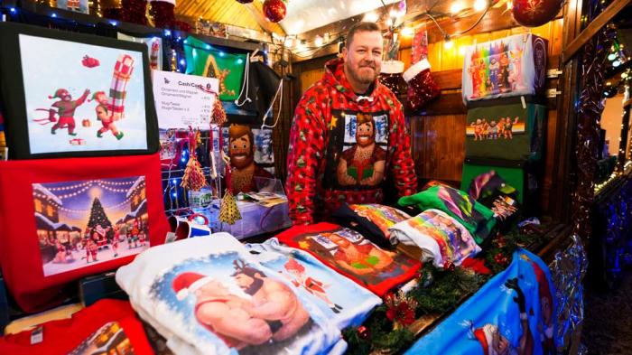 Artist Paul Middleton stands in his shop with shirts he designed at the LGBTQ+ Christmas market "Christmas Avenue" at Nollendorfplatz the for in Berlin, Germany, Monday, Nov. 25, 2024